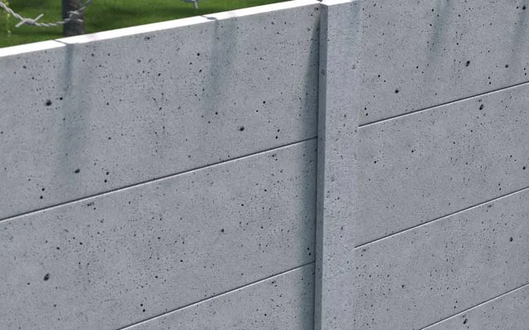 Grey industrial concrete fence with smooth panels and barbed wire above it