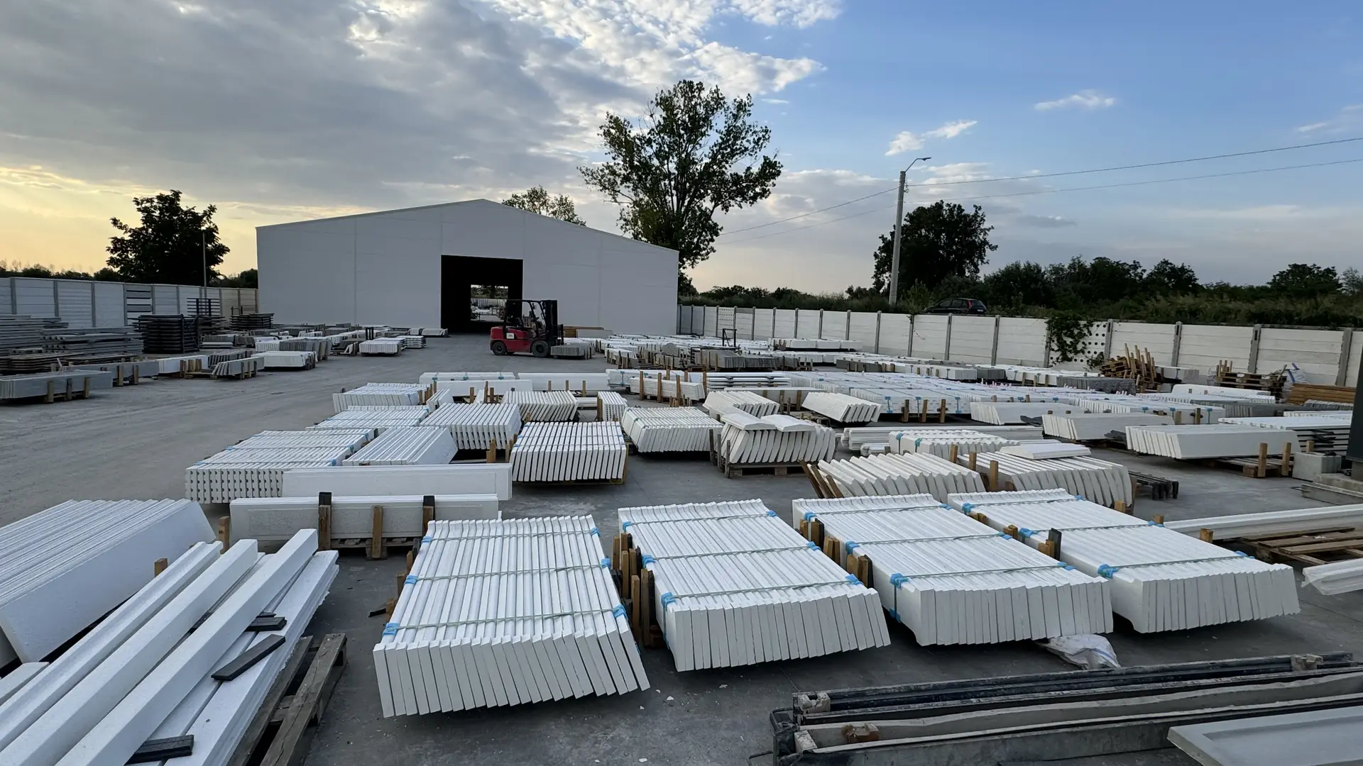 The Konkret Line factory yard in Măgurele at dusk: finished white panels on pallets in front of the production hall