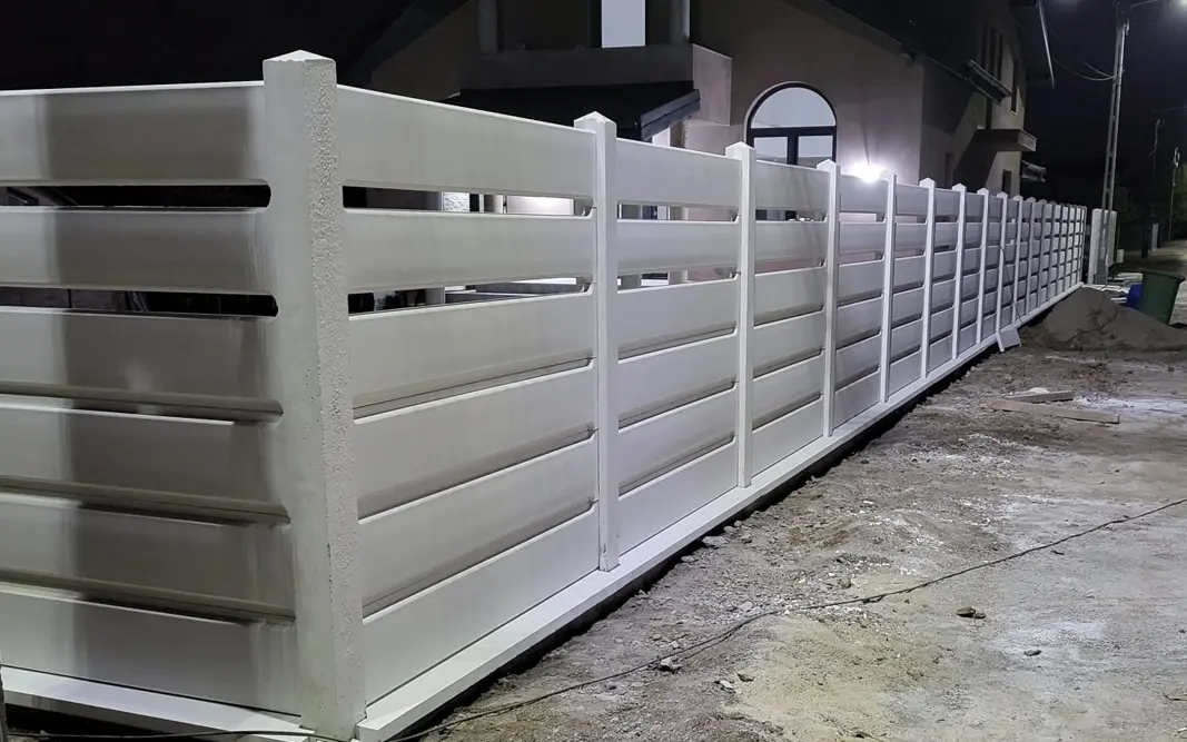 White concrete fence with horizontal panels in front of a house, photographed in the evening