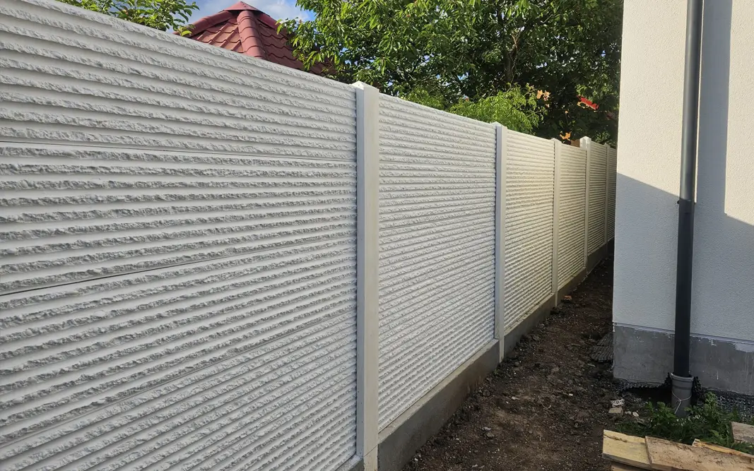 White concrete fence with relief panels alongside a house