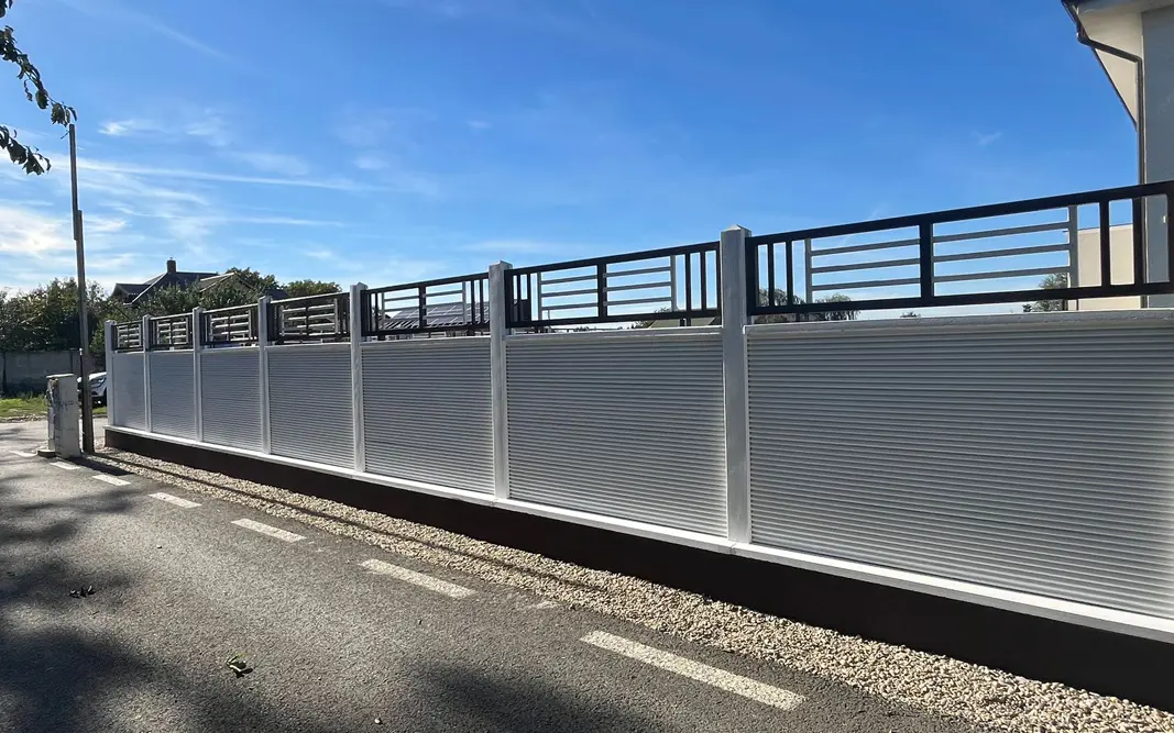 White concrete fence with a metal grille above the panels, along a street