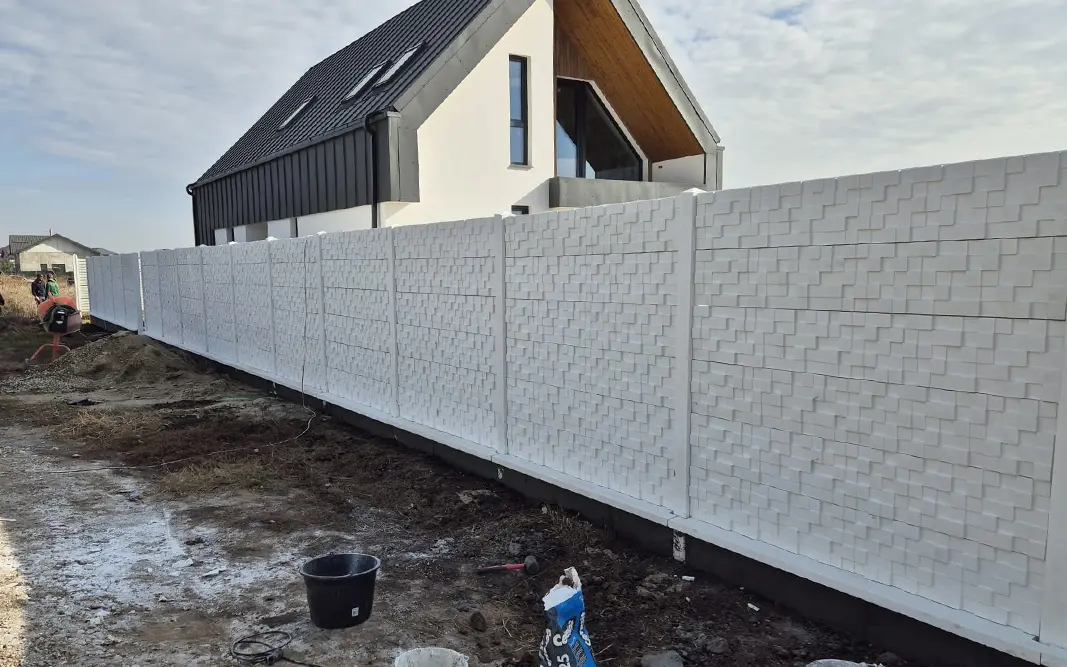 White concrete fence with a geometric relief in front of a modern house